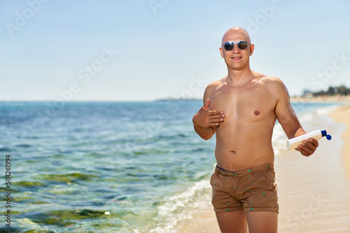 Handsome sexy man relaxing near hotel pool applying sunscreen cream. Summer vacation sea sun tan concept