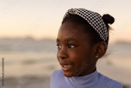 Close-up of smiling african american cute girl looking away against sea and clear sky during sunset