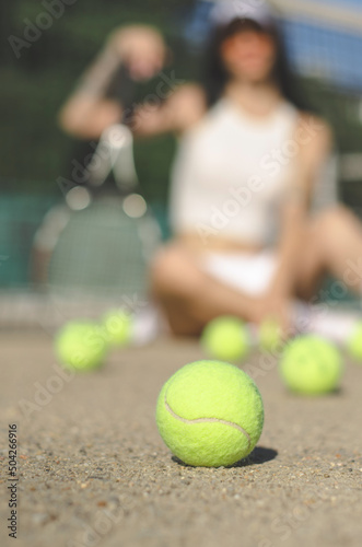 A close-up tennis ball lies on the court against the background of an unrecognizable tennis player. Selective focus. © Анастасія Шатирова