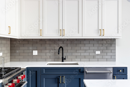 Detail shot of a kitchen with blue and white cabinets,  black faucet, and a subway tile backsplash. photo