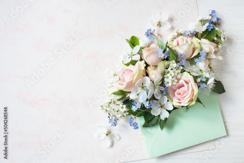 Bouquet of pink roses, white cherry plum flowers, forget-me-nots in an envelope, paper for text. Congratulation card for Mother's Day, wedding and other holidays.