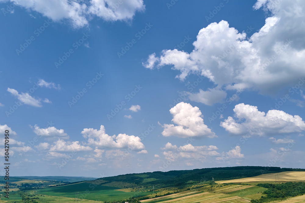 Aerial landscape view of clear blue sky over green cultivated agricultural fields with growing crops and distant woodland on bright summer day