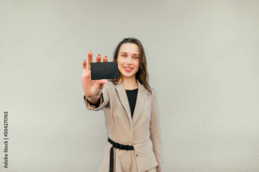 Positive woman in a beige suit shows a black bank card to the camera on a beige background. Copy space. Lady and debit card. Positive woman in a beige suit shows a black bank card to the camera on a beige background. Copy space. Lady and debit card.