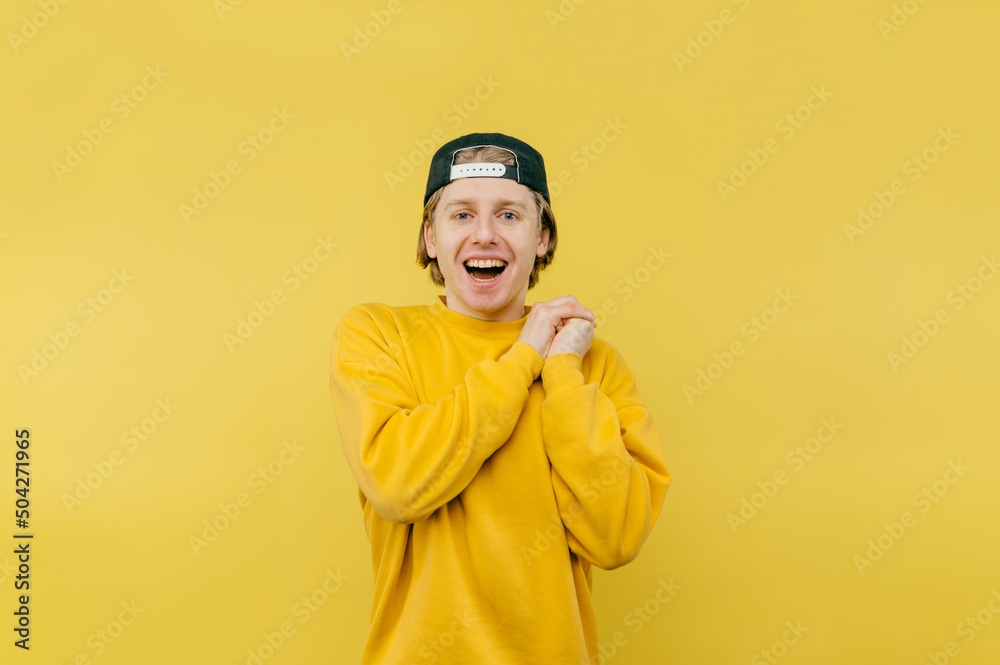 Joyful young man in a cap stands on a yellow background, looks at the camera and laughs. Joyful young man in a cap stands on a yellow background, looks at the camera and laughs.