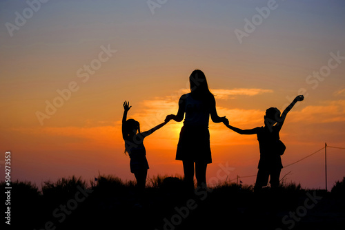 Mother and children hold hands in the background of the sunset.