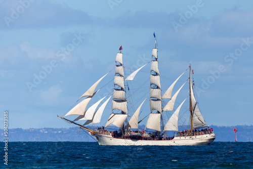 Historic clipper sailing ship on open blue water in full sail.