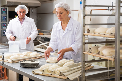Skilled female baker flattening and shaping dough on floured surface before baking
