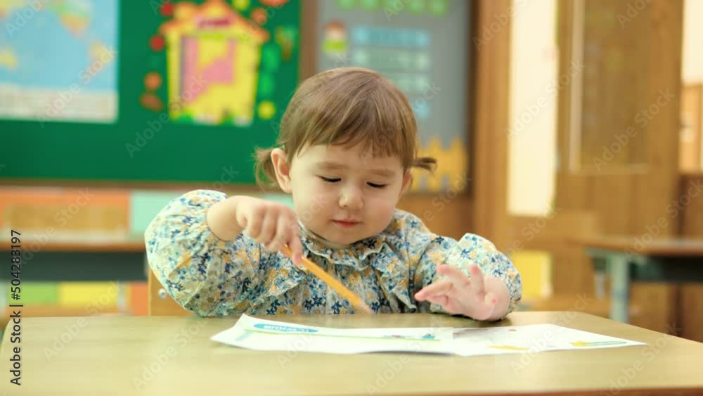 Toddler girl drawing with pencil on the paper in the classroom alone. Kid studying and education concept. 2 yeas old child girl in class Toddler girl drawing with pencil on the paper in the classroom alone. Kid studying and education concept. 2 yeas old child girl in class