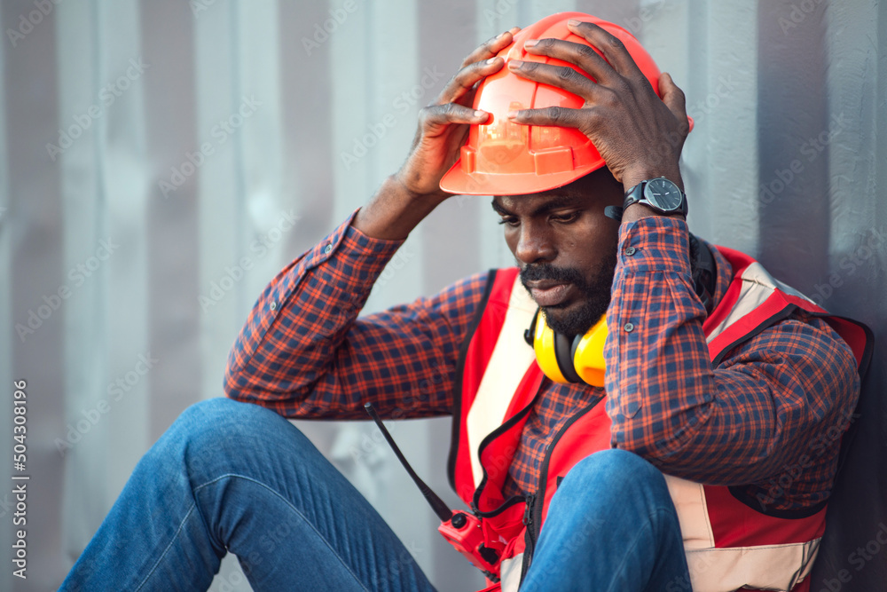 African American male technician or engineer. Sit near a container and look tired and sleepy or unemployed. Logistics industrial cargo mover concept.