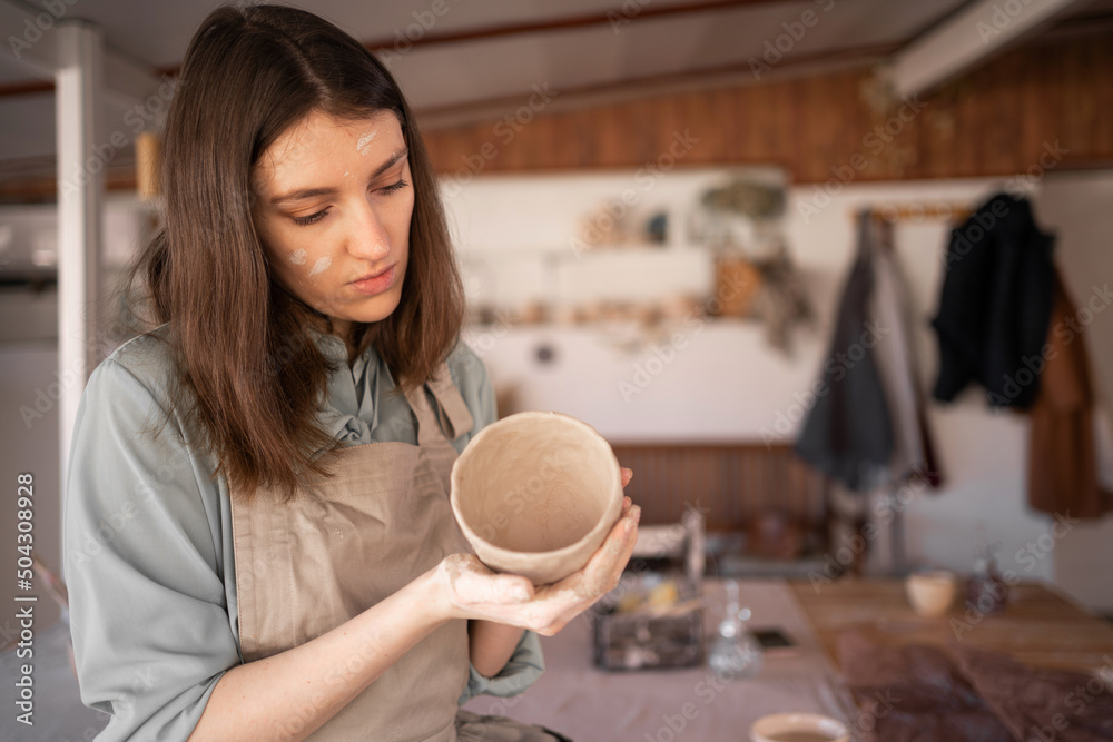 female ceramic business owner makes crafts for sale, young craftswoman sculpting a raw clay bowl during a pottery class at a creative studio. handmade pottery retail store.