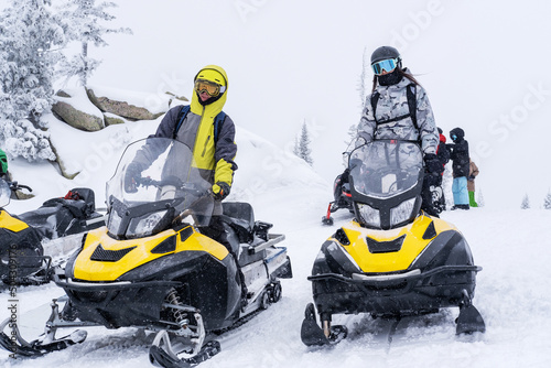 Woman and guy on snowmobiles in winter mountain landscape