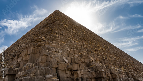 The Great Pyramid of Cheops in Giza. A triangular peak on a background of blue sky and clouds. Huge bricks of ancient masonry are visible. Egypt