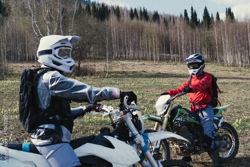 Girls wearing moto equipment sitting on enduro motorcycles during trip through the forests and off-road fields