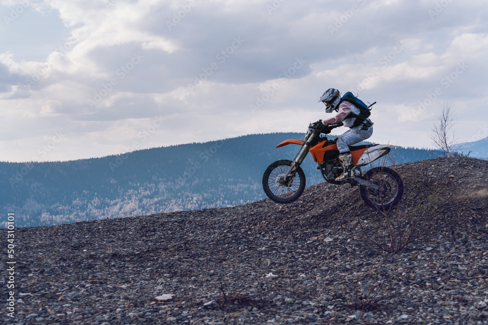 Motorcyclist jumping on motorcycle on mountain top with stunning views of mountains valley
