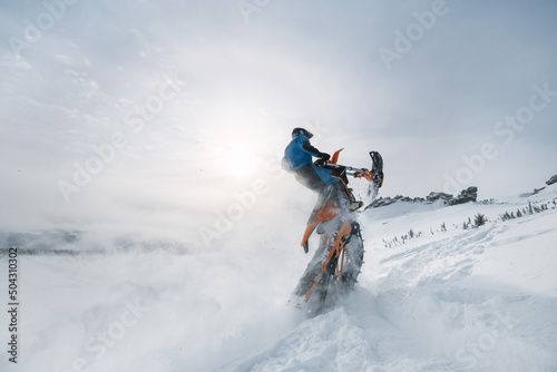 Silhouette of Jumping Snowbike driver in mountain valley in beautiful snow powder during sunse