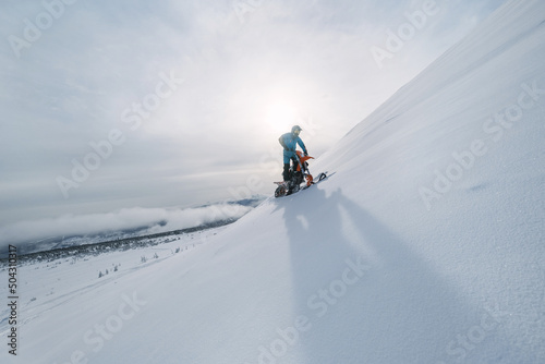 Silhouette of snowbiker on steep slope in sunset rays