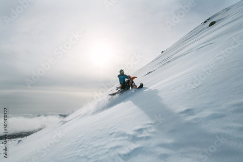 Silhouette of Snowbike rider riding on steep snowy slope on mountain tope above skyline