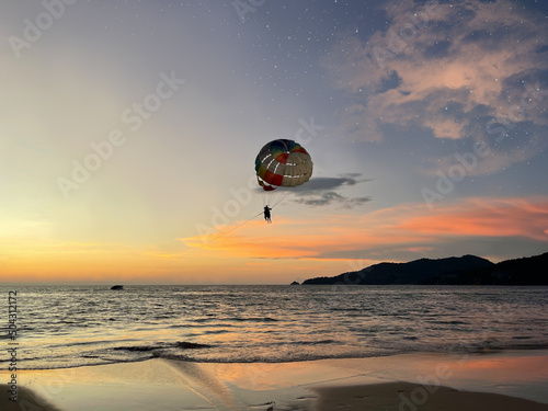 Beautiful sunset above sea. Clouds, stars and moon on the dark night sky. Beach activity. Water sport entertainment. Parasailing. Parachute and people flies in the skies. Fly, fun, enjoy.  Vacation