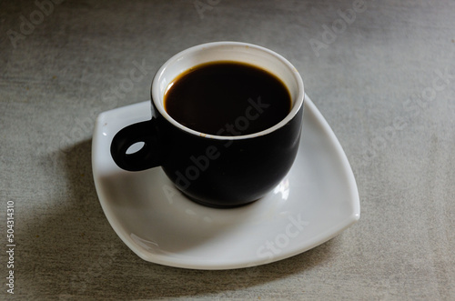 Hot espresso in a black cup on a gray background.