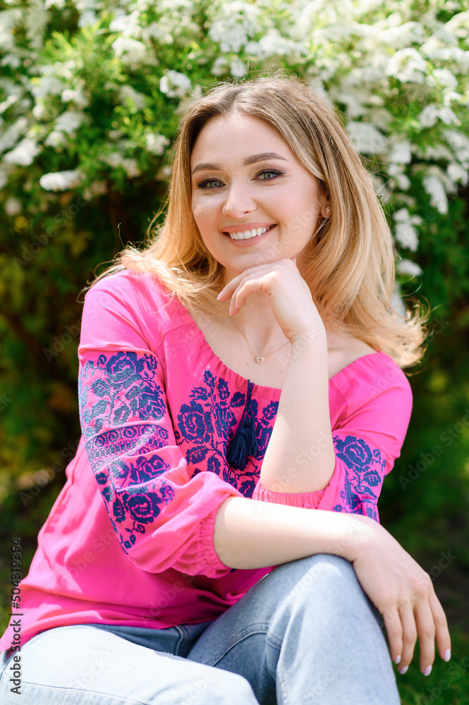 Beautiful blonde hair girl in a pink shirt sitting on the background of a flowering bush