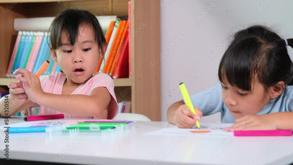 Little girl coloring with her friends sitting in the classroom. Two little sisters taking lessons for homeschooling. Elementary school children enjoy learning together. Back to school