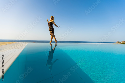 An attractive young woman stands near the pool with a panoramic view.
