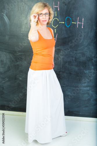 Canvas Print teacher wearing orange blouse, long white skirt and glasses is standing near cha