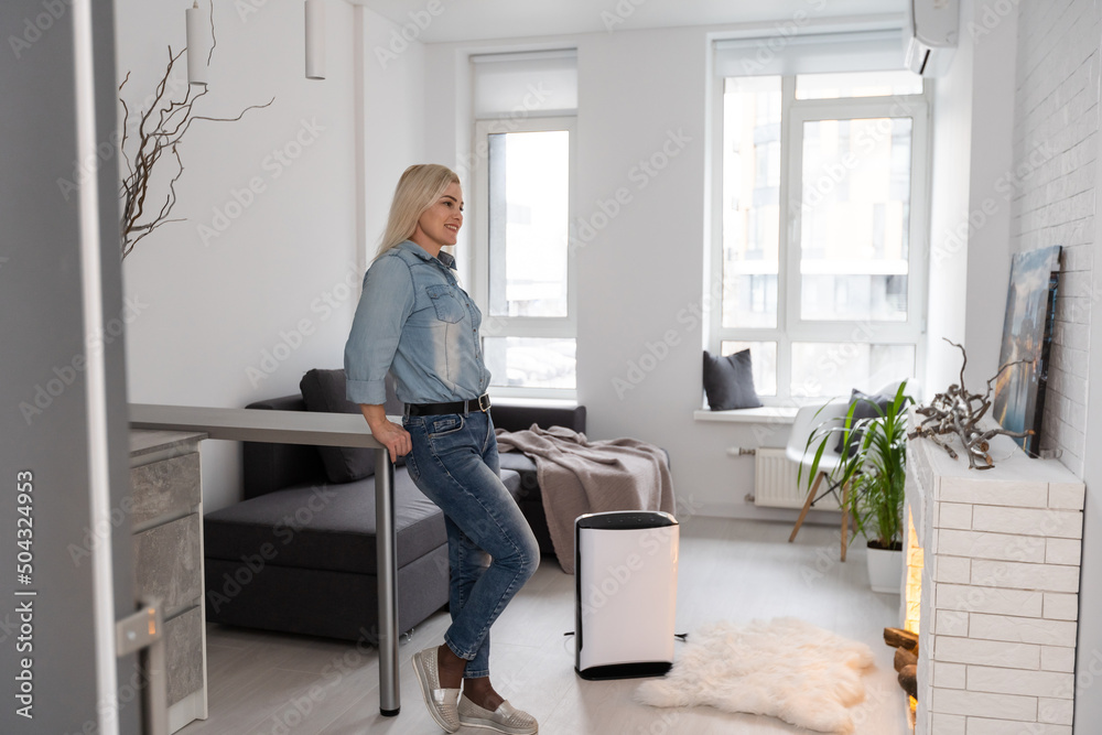 Woman at home in a clean and safe environment from virus by air purifying filter. Woman at home in a clean and safe environment from virus by air purifying filter.