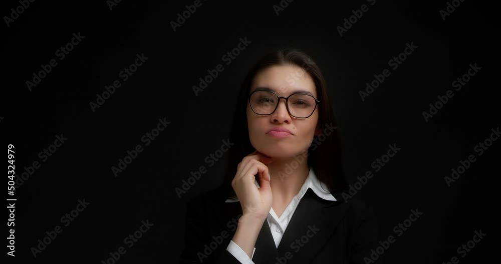 Thoughtful business smart woman in a black jacket is considering a solution to the problem. Asian woman with long dark hair came up with an idea, and she shows her index finger up. Black background Thoughtful business smart woman in a black jacket is considering a solution to the problem. Asian woman with long dark hair came up with an idea, and she shows her index finger up. Black background