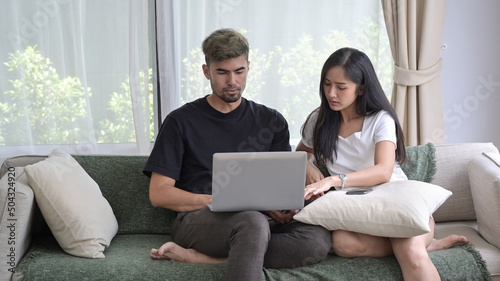 Loving asian couple relaxing on couch and surfing internet with computer laptop.