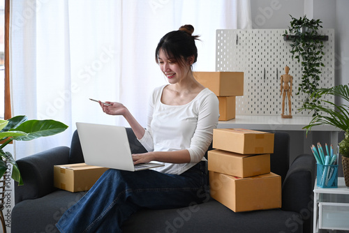 Young asian woman checking product purchase order on laptop and preparing parcel for delivery. © Prathankarnpap
