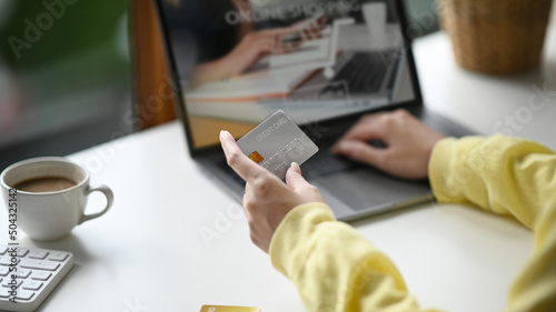 Cropped shot woman holding credit card and using internet banking service on computer laptop.