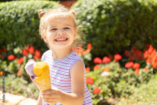 Funny blonde girl in colorful dress eating ice cream in waffle cone. Summer food