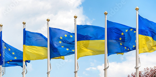 Ukraine and European Union flags on poles fluttering by wind on blue sky. Ukrainian flag panorama photo