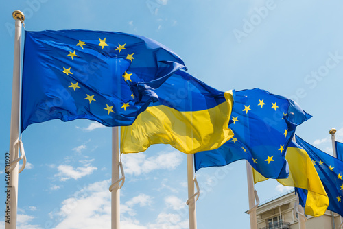 Ukraine and European Union flags on poles fluttering by wind on blue sky. Ukrainian flag photo