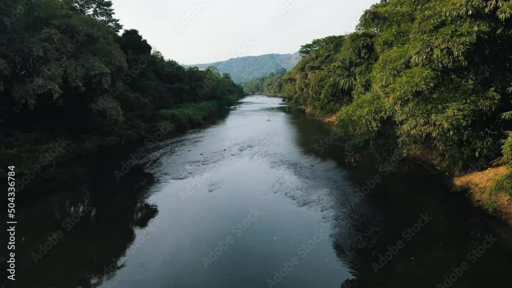 Gently flowing kandy river with beautiful reflections on the water from the green trees along the river side while the wind ripples in the background on a cloudy day. Close up drone dolly shot Gently flowing kandy river with beautiful reflections on the water from the green trees along the river side while the wind ripples in the background on a cloudy day. Close up drone dolly shot