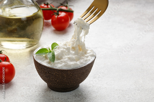 Stracciatella cheese on grey background with fork, oil, basil and tomatoes. Curd cheese product.