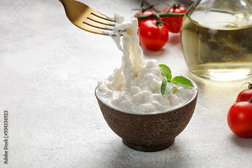 Stracciatella cheese on grey background with fork, oil, basil and tomatoes. Curd cheese product.