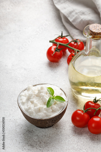 Stracciatella cheese on grey background with oil, basil and tomatoes. Curd cheese product.