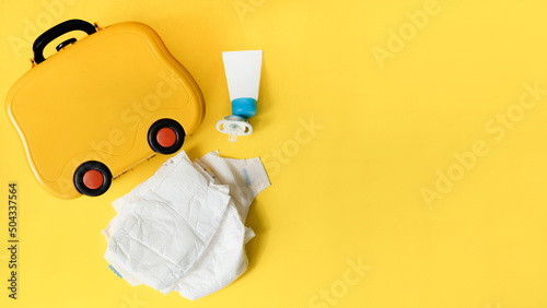 Yellow children's suitcase for travel, next to the cream, pacifier and diapers. The concept of traveling with a child. Copy Space. photo