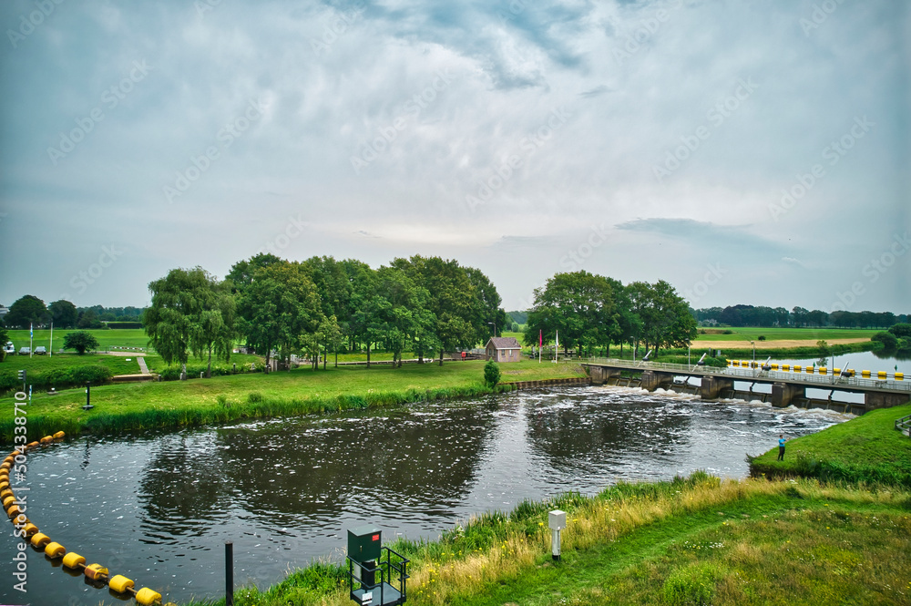 Drone view of the river Vecht, green grass, trees, beautiful blue sky and cycle path through the Vecht valley. Bridge and weir in the river. Dalfsen Netherlands