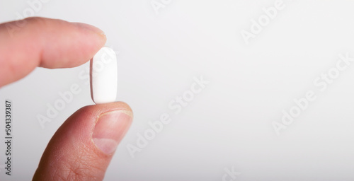 A man holds a white pill in the palm of his hand, close-up