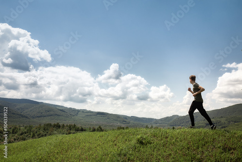 Light-skinned male runner running from grass top of mountain hill. Healthy man jogging 