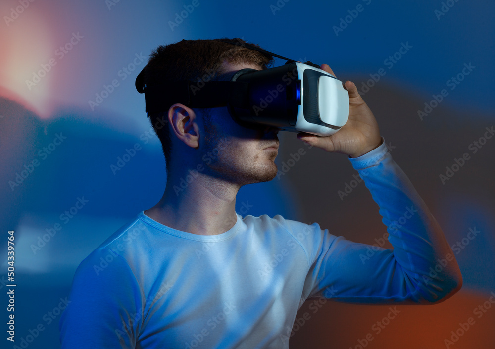 Modern young man experiencing virtual reality glasses in futuristic neon illuminated studio Modern young man experiencing virtual reality glasses in futuristic neon illuminated studio