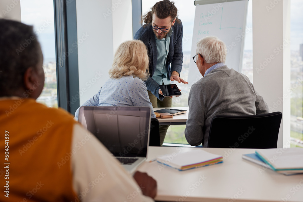 Obraz premium A young educator in classroom showing to senior students lesson on tablet.