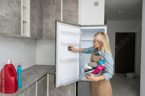 Young Woman Cleaning Refrigerator With Rag At Home.