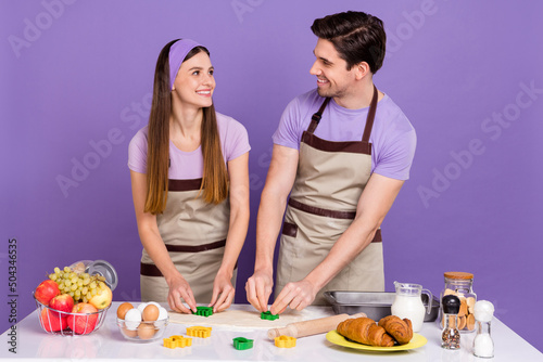 Portrait of two idyllic positive people make cookies shape dough isolated on purple color background