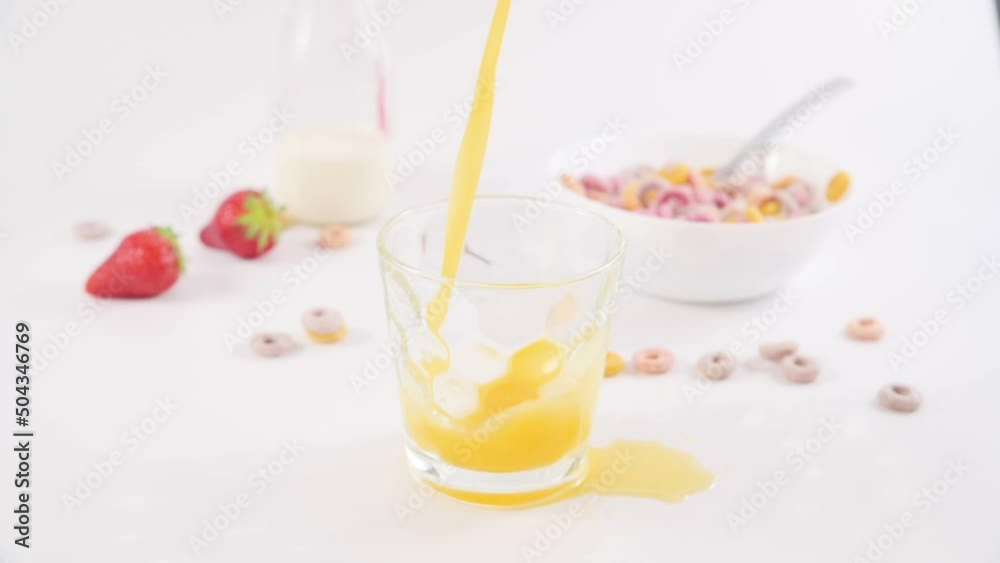 Glass with orange juice. Juice is poured into a glass on a light background. Vitamin breakfast and healthy. Next to it is a bowl of cereal. slow motion. High quality FullHD footage