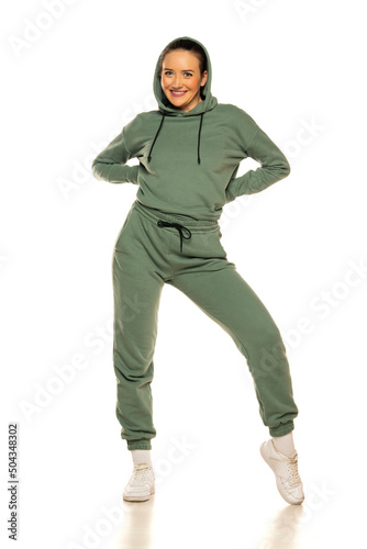 Front view of a young happy woman in a green tracksuit and hood posing to a white background in the studio