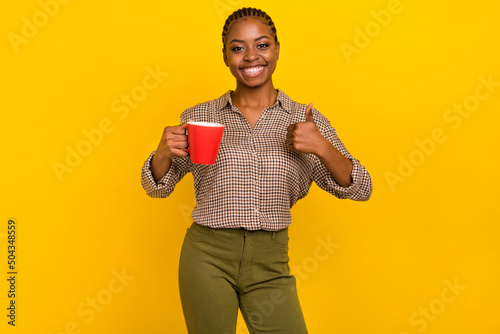 Photo of adorable confident lady dressed checkered shirt holding tea cup thumb up isolated yellow color background